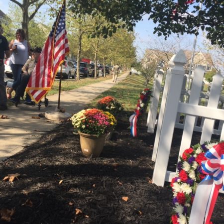 The American flag to the left of fenced off area with two wreaths of red, white, and blue flowers