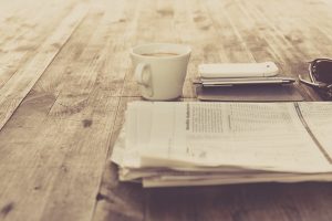 A folded newspaper next to a cup of coffee on a worn tabl